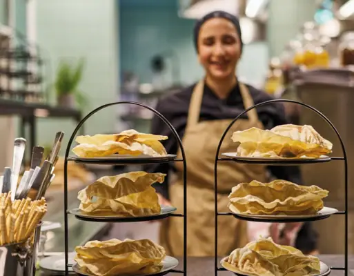 Etageren Auntie Heidi Zwei Etageren stehen in einer Küche und eine Köchin steht dahinter mit einer Schürze um.