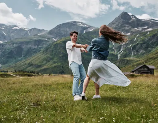 Sommer in den Bergen Ein Mann und eine Frau tanzen auf einem Feld mit Bergen im Hintergrund.