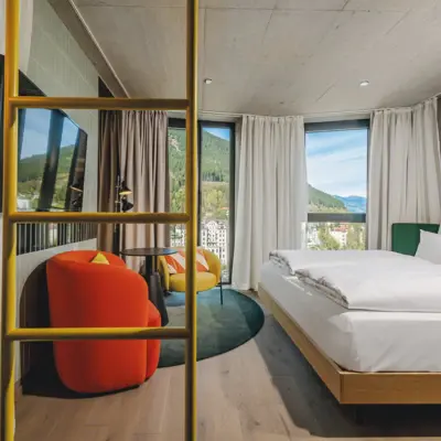 Ausblick inklusive – Stylisches Zimmer mit Bergblick in Bad Gastein Helles Designhotel-Zimmer mit Panoramafenstern, moderner Einrichtung, bunten Sesseln und Blick auf die Bergwelt von Bad Gastein