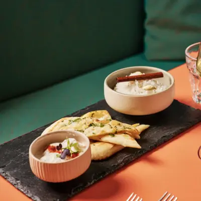 Auntie Heidi Vorspeise Eine Vorspeise mit Brot und Dips ist auf einem Schieferbrett angerichtet.