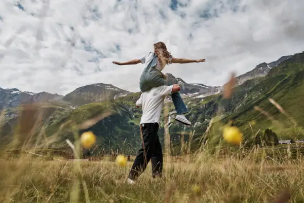 Ein mann trägt eine Frau in einer Berglandschaft auf den Schultern. Ein Mann trägt eine Frau auf seinen Schultern in einem grasbewachsenen Feld.