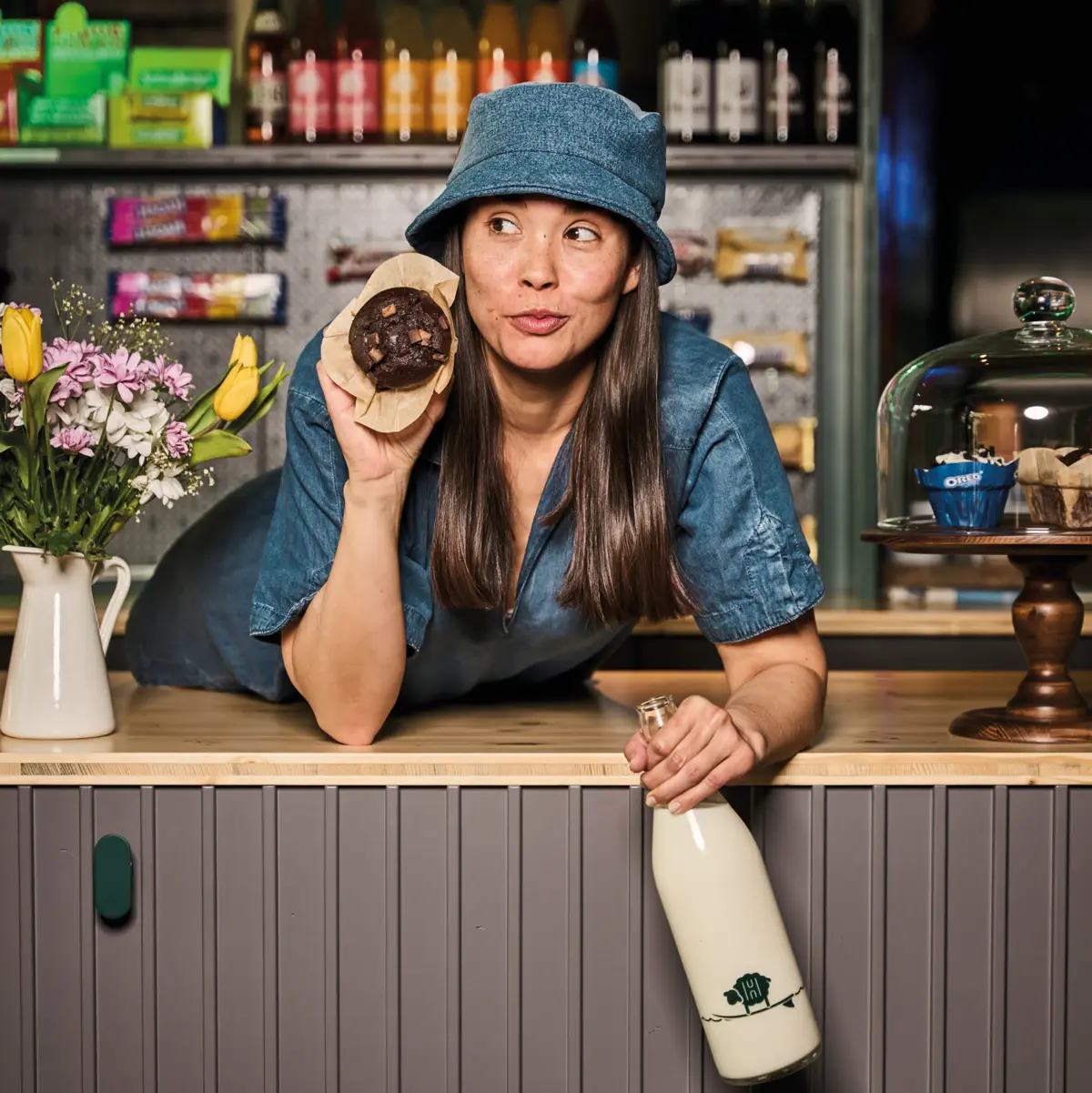 Muffin Store and Stuff Eine Frau lehnt sich auf eine Theke und hält einen Muffin in der Hand.
