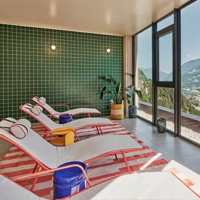 Ruheraum im Alpine Swim Club Heller Ruheraum mit stylischen Liegen, farbenfroher Einrichtung und Panoramafenster mit Blick auf die Berge von Bad Gastein