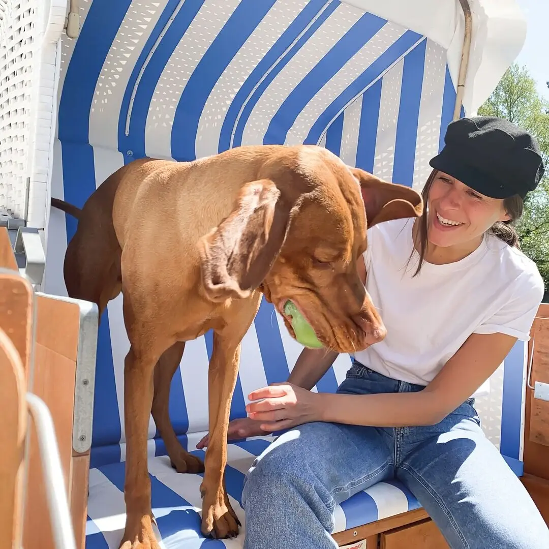 Hundestrandkorb St. Peter-Ording Eine Frau sitzt mit einem großen braunen Hund in einem Strandkorb und lächelt.
