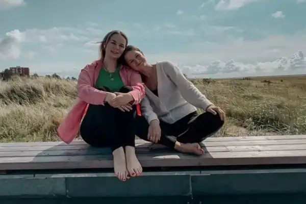 Yoga Retreat St. Peter-Ording mit Mia und Johanna Die Yoga-Lehrerinnen Mia und Johanna sitzen auf einer Bank im Freien unter einem bewölkten Himmel.
