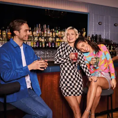 Drifters Hang Out im Urban Nature Hotel im Badeschloss in Bad Gastein Drei junge Erwachsene genießen bunte Cocktails an einer stilvollen Hotelbar