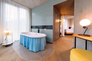 Juniorsuite Panoramablick Badezimmer mit Badewanne und einem Schlafzimmer mit Bett im Hintergrund.