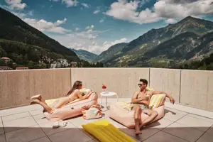 Liegenbereich Ein Mann und eine Frau auf einer Terrasse mit Bergblick.