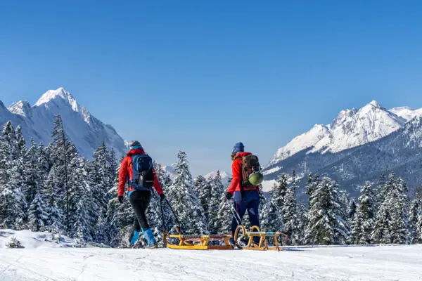 Rodeln Bad Gastein Zwei Menschen wandert auf einem verschneiten Berg und ziehen Schlitten hinter sich her.