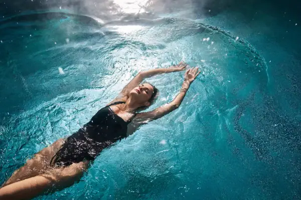 Alpine Swim Club Eine Frau in einem schwarzen Badeanzug schwebt auf dem Wasser.
