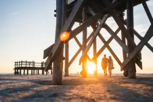 Strand Ein Paar spaziert am Strand unter einer Holzstruktur.