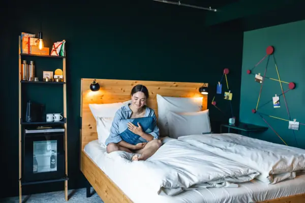 Zimmer im Urban Nature St. Peter-Ording Eine Frau sitzt auf einem Bett in einem Zimmer im Urban Nature Hotel St. Peter-Ording und hält ein Kissen in ihren Armen.