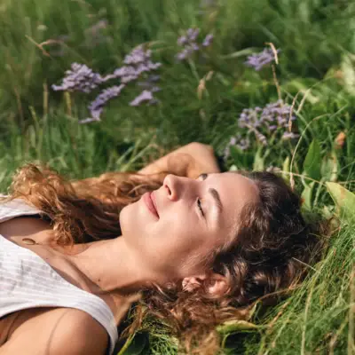Nachhaltigkeit Urban Nature St. Peter-Ording Eine Frau liegt mit geschlossenen Augen im Gras und lächelt.