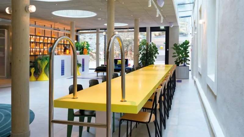 Lobby im Urban Nature Hotel im Badeschloss Bad Gastein Kreatives Interior im Hotel:Modern gestalteter Rezeptionsbereich mit Schwimmbadleiter als Designelement, gelb-weißen Akzenten und stilvollen Sitzgelegenheiten.