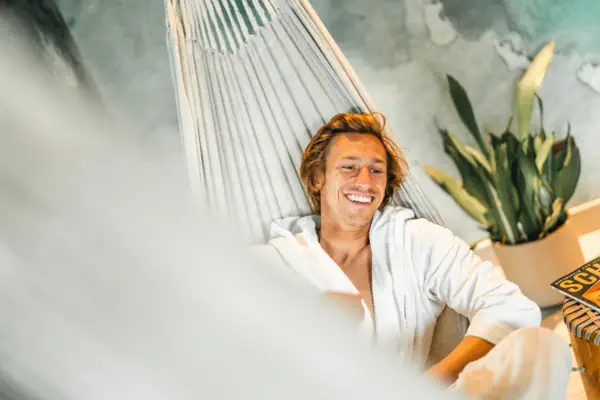 Day Spa Urban Nature St. Peter-Ording Ein Mann im Bademantel liegt lächelnd in einer Hängematte.