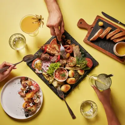 Kulinarische Vielfalt in Auntie Heidis Restaurant Bunte Auswahl an regionalen und mediterranen Spezialitäten auf einer gelben Tischplatte mit Brot, Getränken und Vorspeise