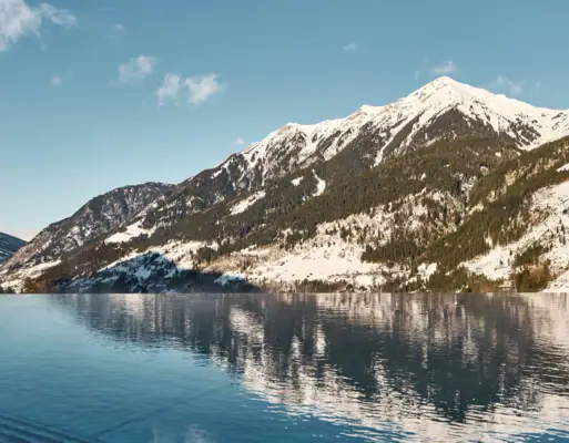 Berge im Winter Ein Gewässer mit schneebedeckten Bergen und blauem Himmel.