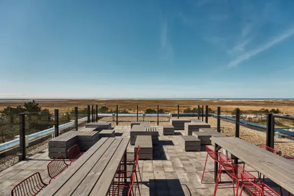 Rooftop-Bar Terrasse Eine Terrasse mit einigen Tischen und Bänken mit Blick auf die Salzwiesen und die Nordsee in St. Peter-Ording.
