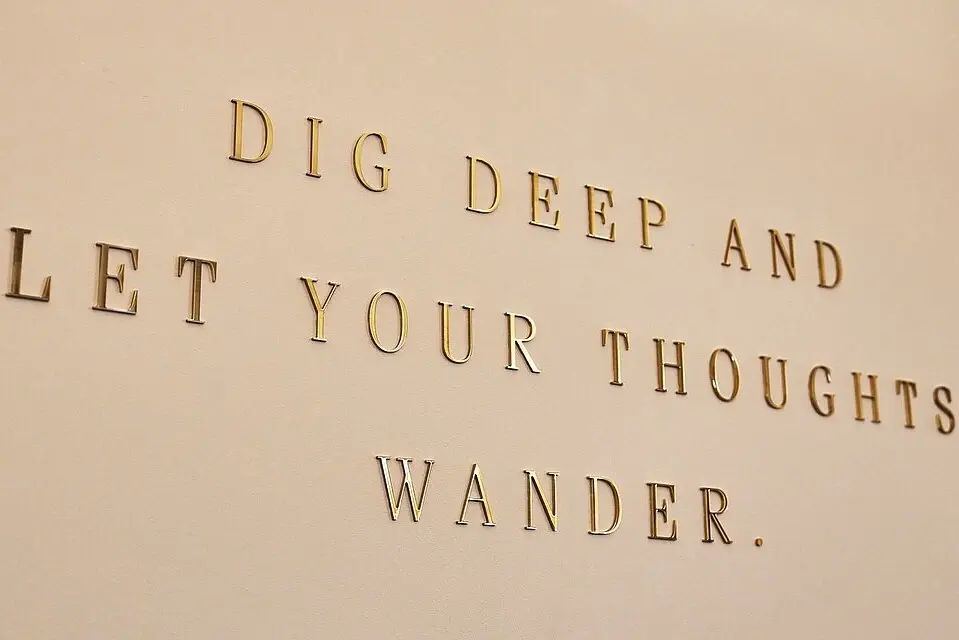 Wandzitat in goldener Schrift Wandzitat in goldener Schrift: „Dig deep and let your thoughts wander“ – inspirierender Spruch in modernem Interieur