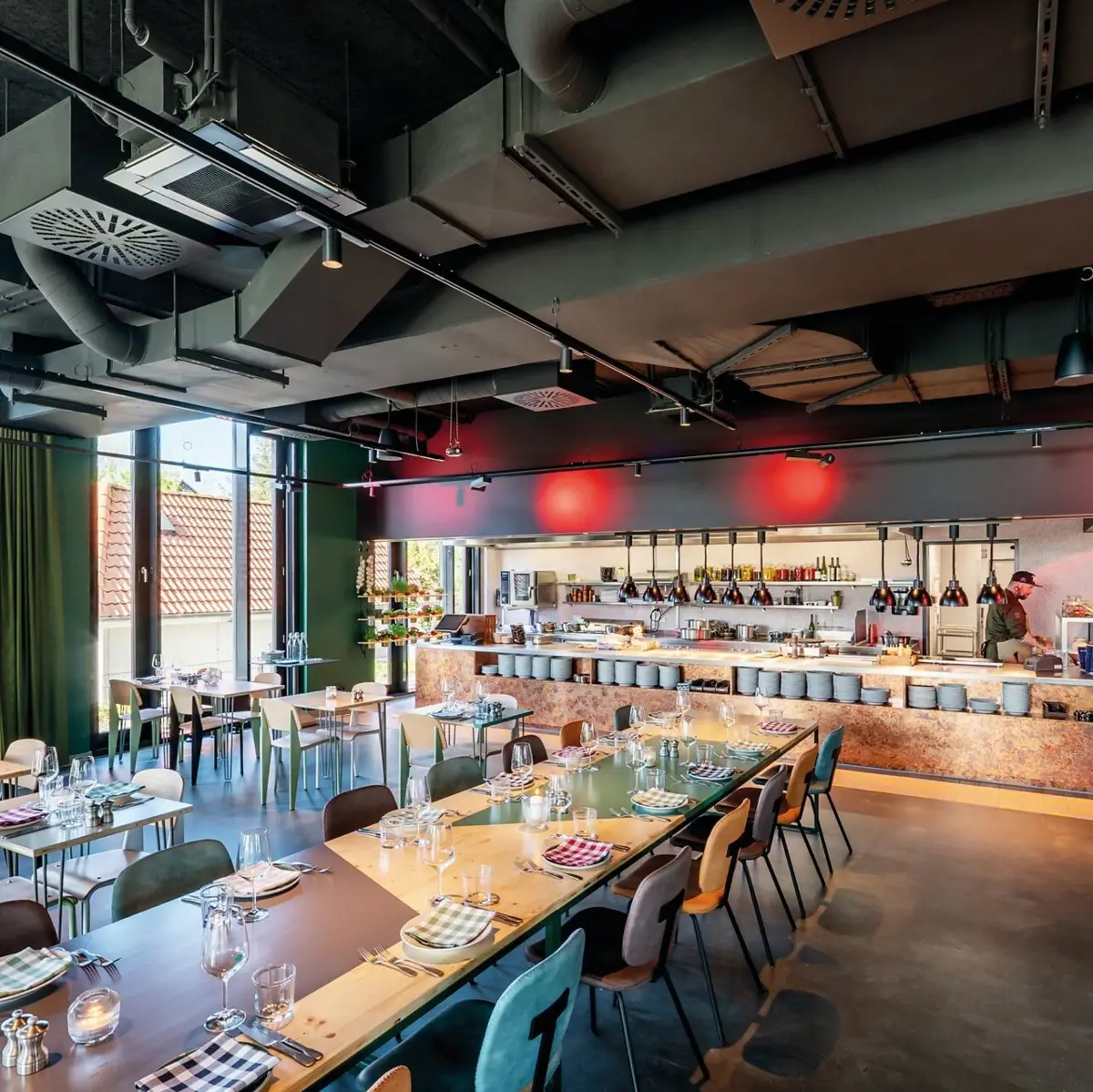 Restaurant Auntie Clara Ein Restaurant mit einer langen Tafel und mehreren gedeckten Tischen und einer offenen Küche im Hintergrund.