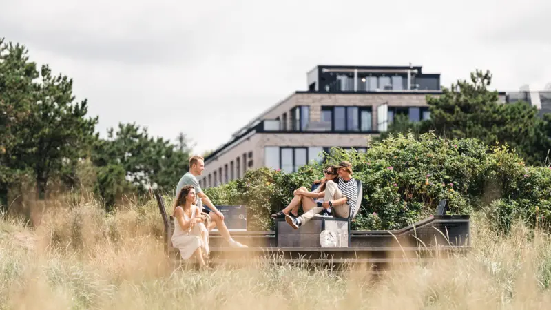 Urban Nature St. Peter-Ording Mehrere Menschen sitzen vor dem Urban Nature Hotel.