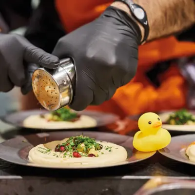 Hummus Auntie Heidi Mehrere Teller Hummus werden von einem Koch angerichtet.