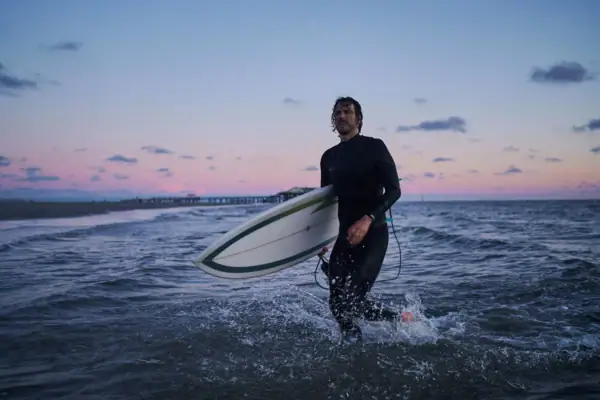 Surfen St. Peter-Ording Ein Mann in einem Neoprenanzug trägt ein Surfbrett im Wasser.
