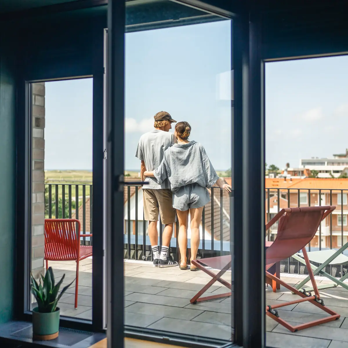 Zimmer Urban Nature St. Peter-Ording Zwei Personen stehen auf einem Balkon und blicken aus einem Fenster.
