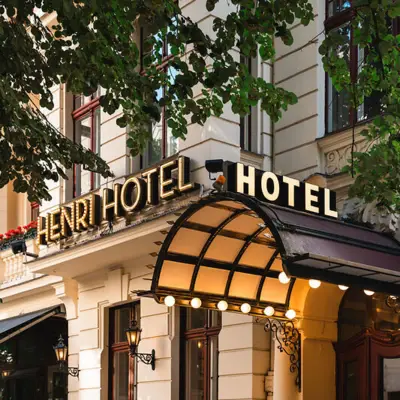 HENRI Hotel in Berlin Eingang des HENRI Hotels in Berlin mit klassischem, eleganten Schriftzug und begrüntem Vordach, umgeben von alten Bäumen und historischer Fassade