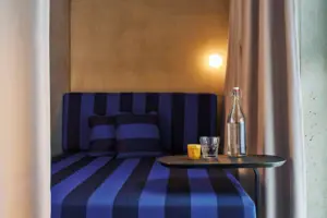 Doppelzimmer Comfort mit Schlafnische Blau-schwarz gestreiftes Sofa mit Glas und Flasche auf einem Tisch.