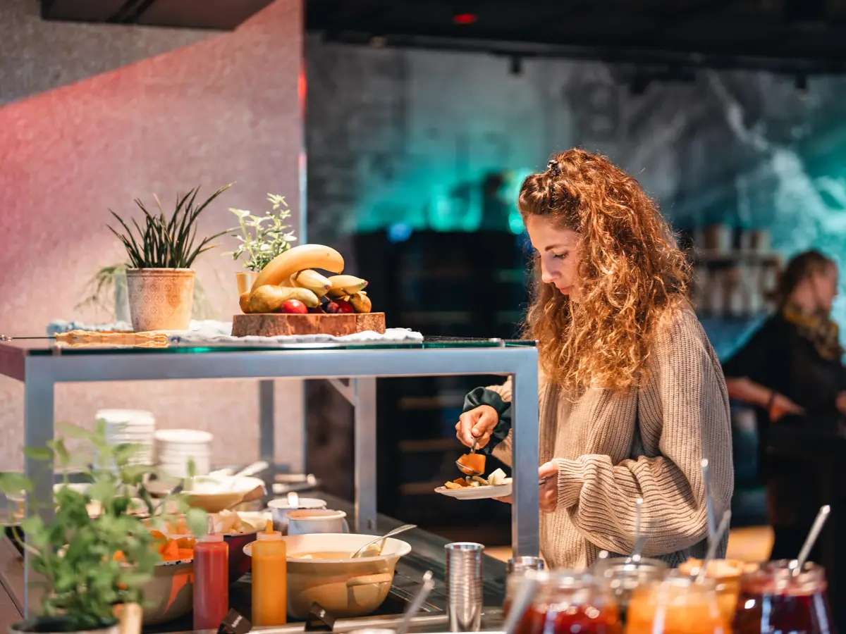 Frühstücksbuffet St. Peter-Ording Eine Frau steht an einem Frühstücksbuffet und tut sich Speisen auf ihren Teller.