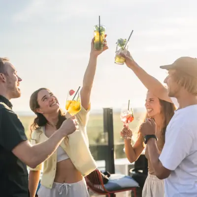 Rooftop Bar Scraper’s Club Eine Gruppe von Menschen steht auf der Rooftop Bar Scraper's Club St. Peter-Ording und stößt mit Getränken in der Hand an.