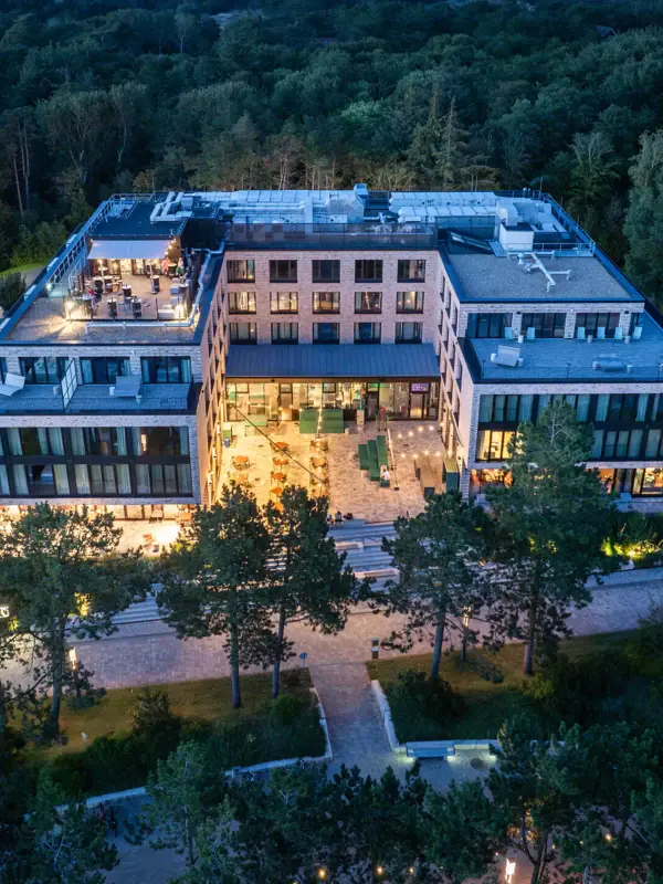 Urban Nature St. Peter-Ording Das Urban Nature Hotel in St. Peter-Ording bei Nacht von oben fotografiert mit Bäumen im Hintergrund.