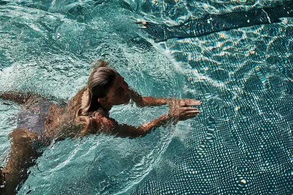 Dip in & swim! Frau schwimmt im türkisblauen Pool
