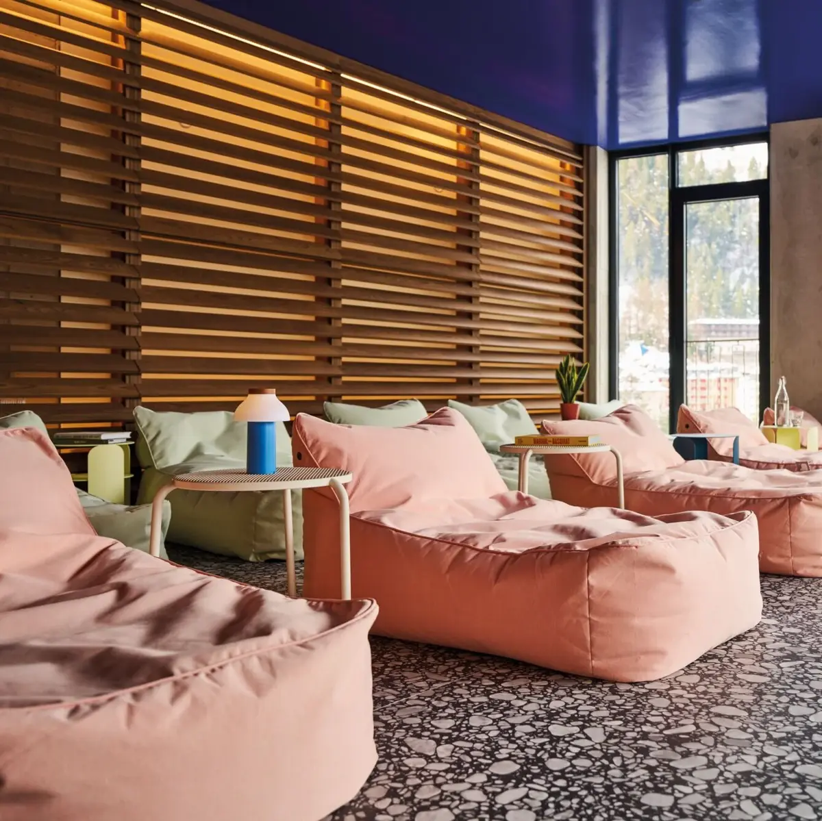 Ruhebereich im Alpine Swim Club Moderner Ruheraum mit gemütlichen Sitzsäcken, stilvollen Beistelltischen und indirekter Beleuchtung vor Holzlamellenwand