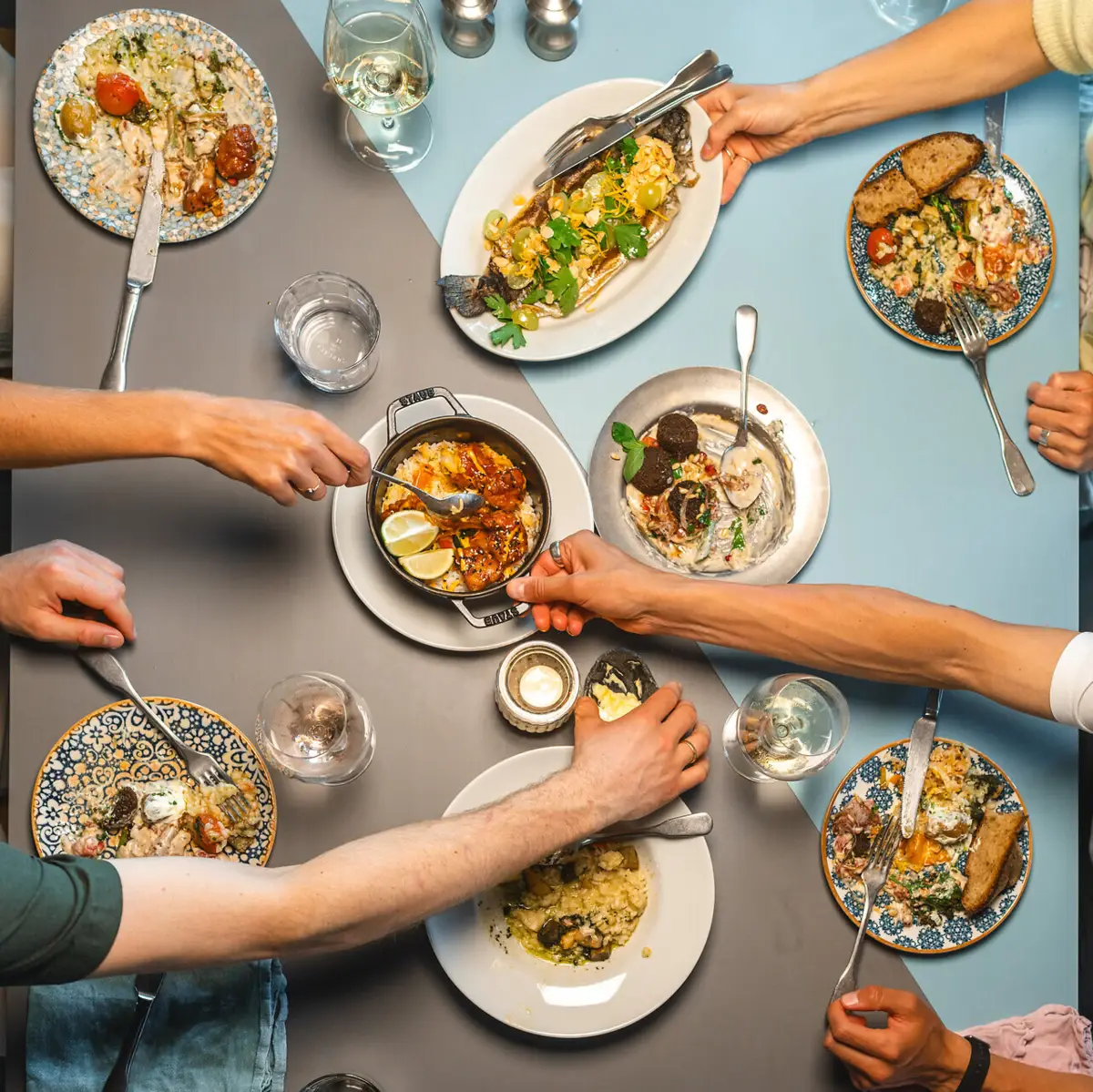 Gastronomie Urban Nature Auf einem Tisch im Auntie Clara Restaurant St.Peter-Ording stehen viele Teller und Vorspeisen in der Mitte, die sich eine Gruppe von Personen teilt.