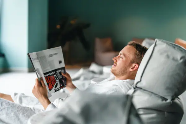 Day Spa im Urban Nature St. Peter-Ording Ein Mann im Bademantel liegt auf einem gemütlichen Sitzsack und liest eine Zeitschrift.