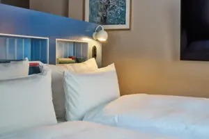 Juniorsuite Ein Bett mit weißen Kissen und einer Lampe.