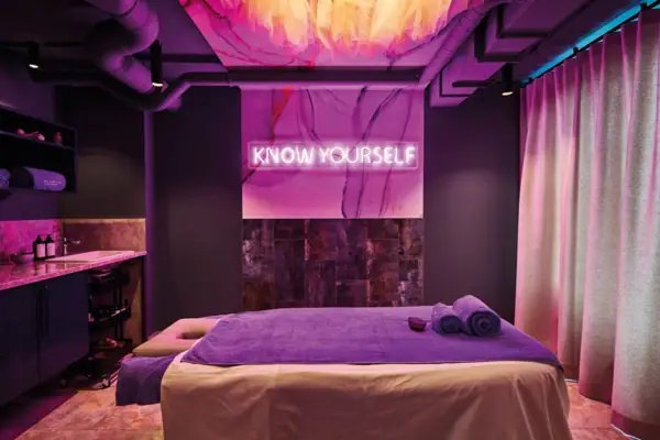 Treatments und Massagen Urban Nature St. Peter-Ording Lila Zimmer mit einer Massageliege und Handtuch im Urban Nature Hotel St. Peter-Ording.