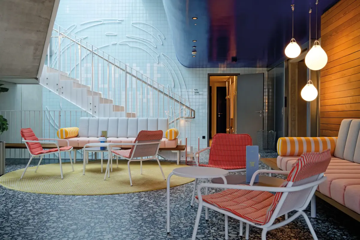 Eingangsbereich Alpine Swim Club Modern gestalteter Loungebereich mit farbenfrohen Möbeln, Rundtreppe, stylischer Wandgestaltung und gemütlichem Lichtkonzept