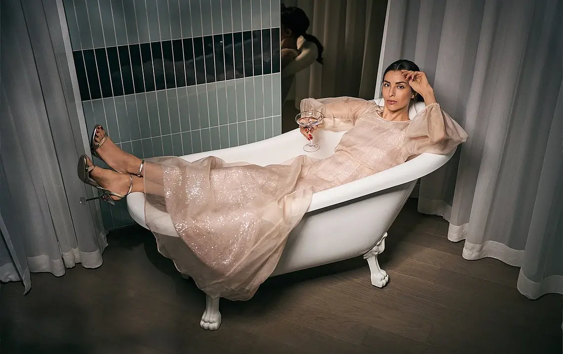 Frau in Badewanne Eine Frau liegt in einem Kleid in einer freistehenden Badewanne und hält einen Drink in der Hand.