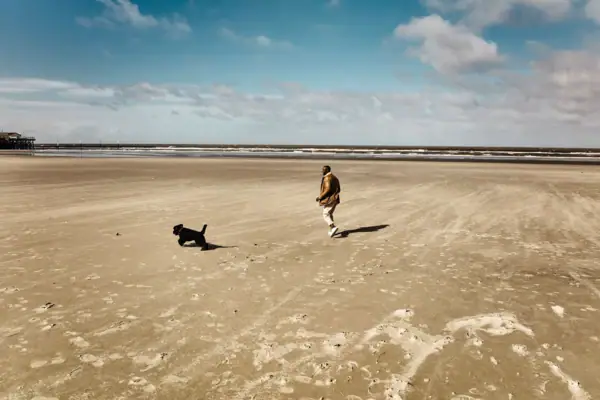 Strand St. Peter-Ording Ein Mann läuft mit einem Hund am Strand von St. Peter-Ording lang.