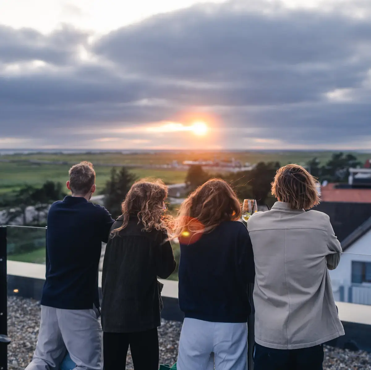 Sonnenuntergang Rooftop Eine Gruppe von Menschen steht auf der Rooftop Bar Scraper's Club St. Peter-Ording mit Blick auf die Salzwiesen und das Meer bei Sonnenuntergang.