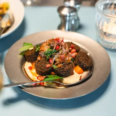 Falafel Auntie Clara Restuarant Ein Teller auf dem einige Falafal-Bällchen auf Hummus hübsch angerichtet sind und mit Granatapfelkernen getoppt.