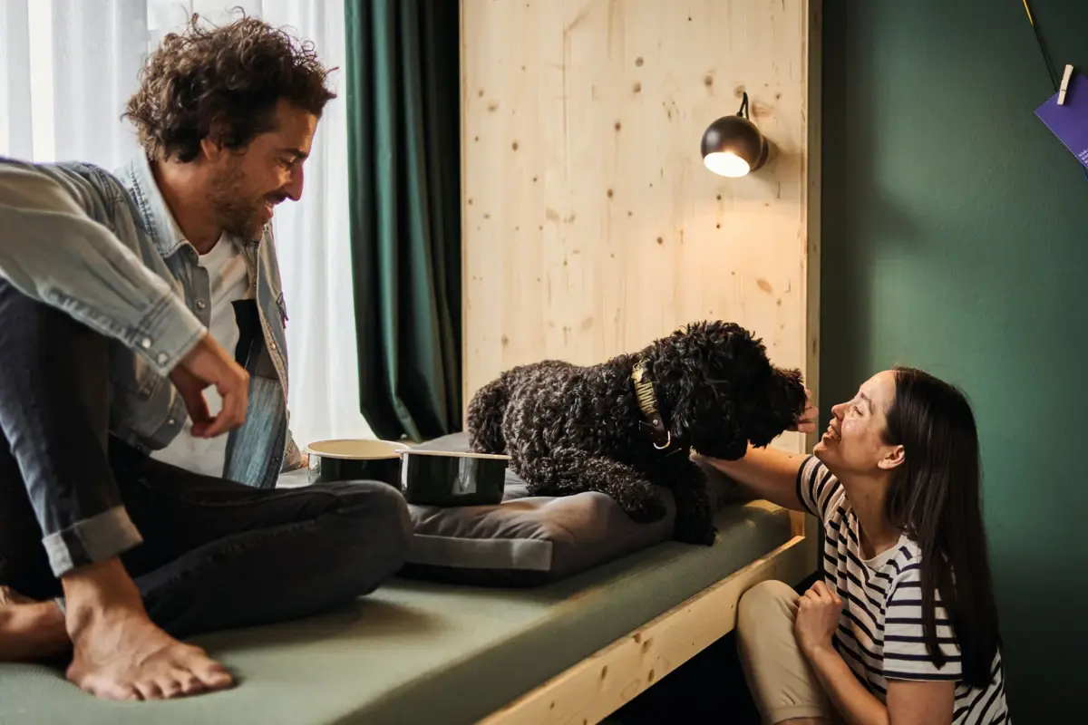 Urban Nature Hund Ein Mann und eine Frau sitzen mit einem Hund auf einem Daybed in einem Hotelzimmer im Urban Nature Hotel St. Peter-Ording.