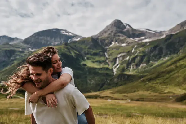 Glücksmomente in den Gasteiner Bergen Junges Paar beim Wandern in den Bergen von Bad Gastein – Frau lacht auf dem Rücken ihres Partners, umgeben von alpiner Natur