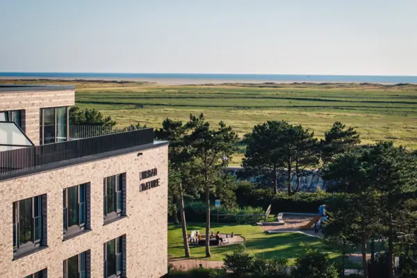 Urban Nature St. Peter-Ording Ein Gebäude mit einem Spielplatz und einem Grasfeld.