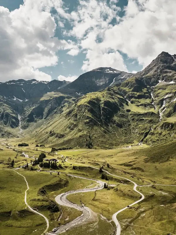 Natur in den Gasteiner Bergen Weitläufige Alpenlandschaft mit grünen Berghängen, kurviger Straße und Bergfluss unter dramatischem Himmel – Naturidylle in der Region Bad Gastein