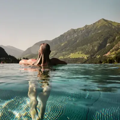 Pool Bad Gastein Eine Frau lehnt sich an den Rand vom Pool und schaut in die Berge.