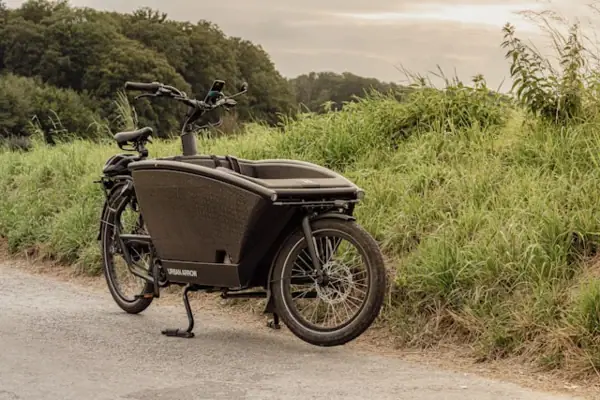 Lastenrad Ein Lastenfahrrad steht am Rand einer Straße neben einem grünen Wall und mit Bäumen im Hintergrund.